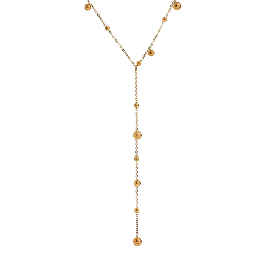 The Orbit Necklace A gold Y-shaped dangle necklace featuring a delicate chain with small spherical beads and a longer central drop ending in larger polished beads, shown against a plain white background.
