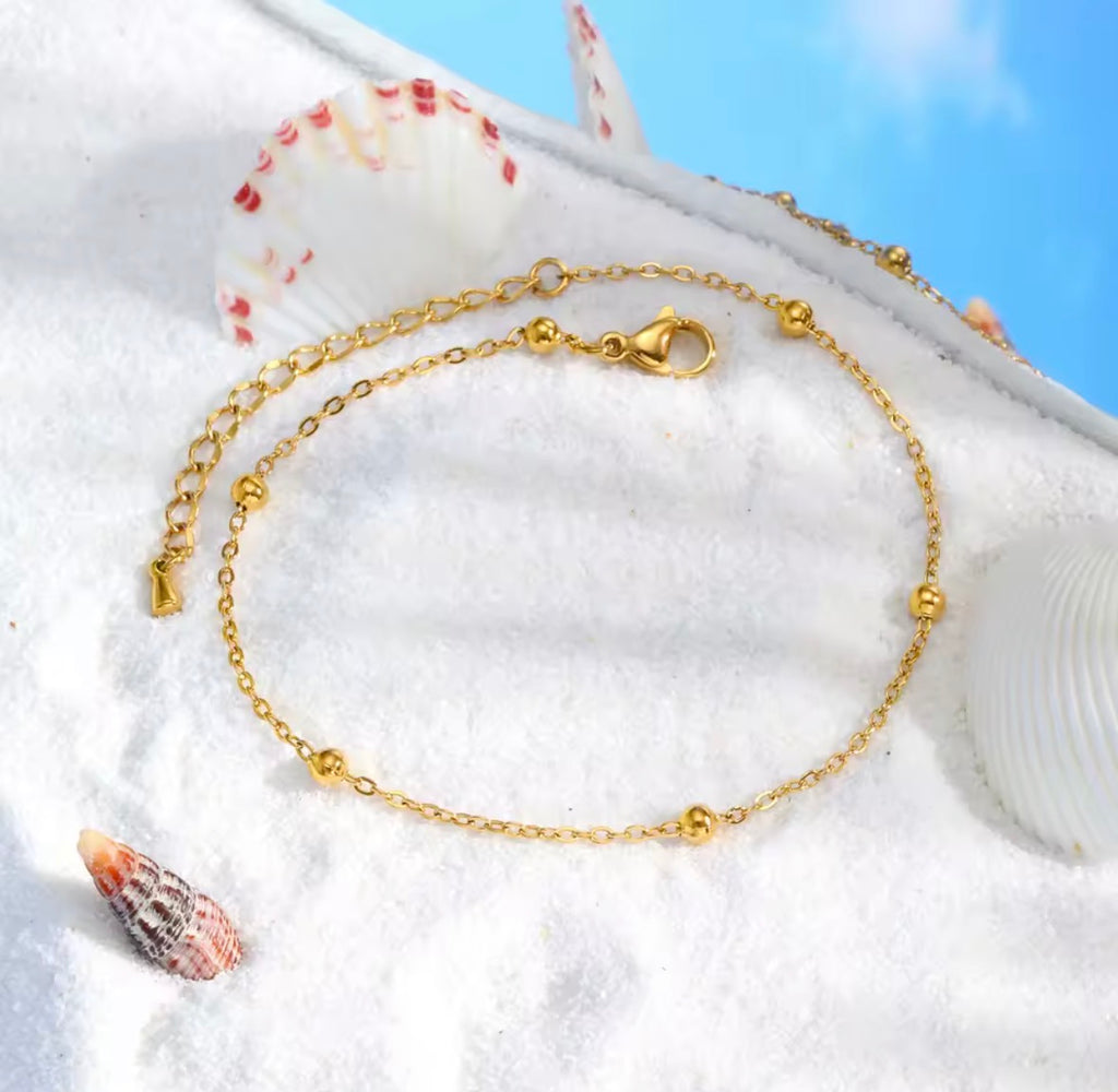 The Oriana Anklet  Gold anklet on a white surface with shells and sand