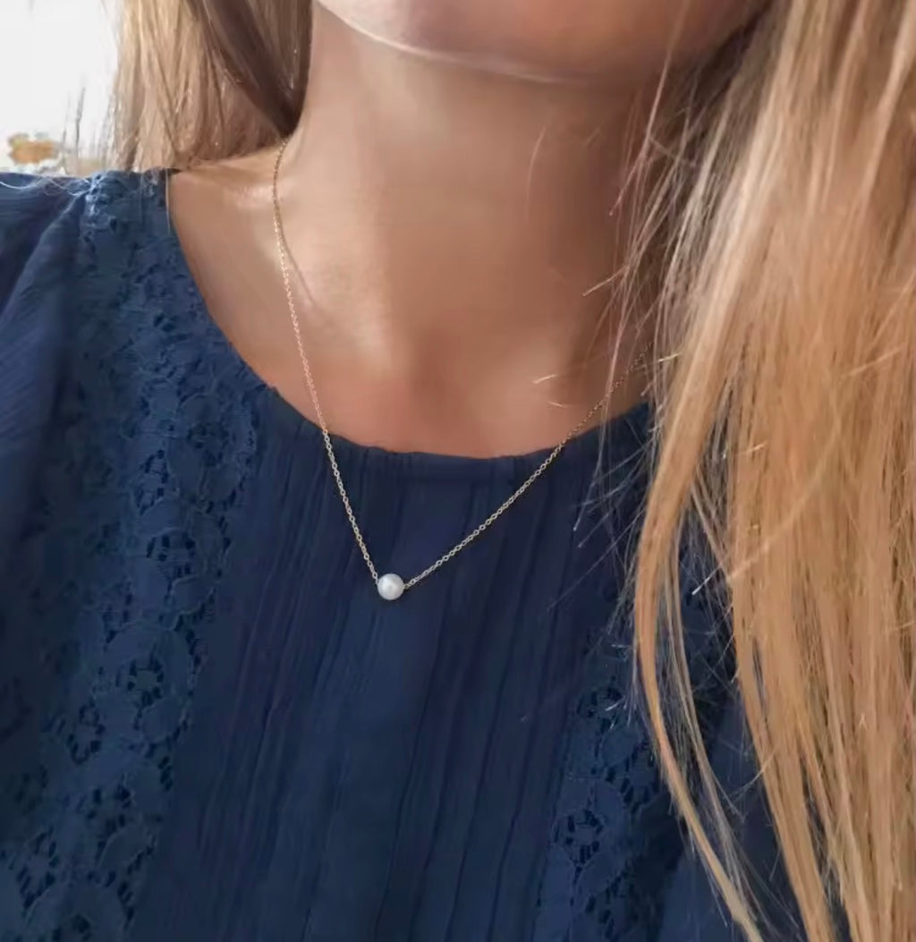 The Perla Necklace Person wearing a blue lace top with a delicate necklace featuring a pearl pendant.
