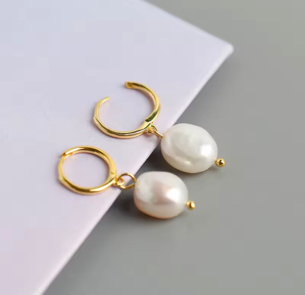 The Perlina Studs  Gold hoop earrings with pearl drops on a light gray surface