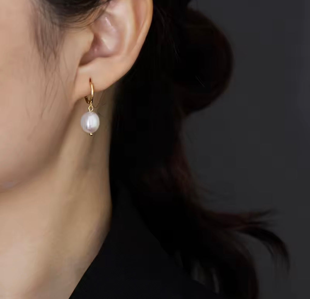 The Perlina Studs  Pearl earring worn by a person with a dark background