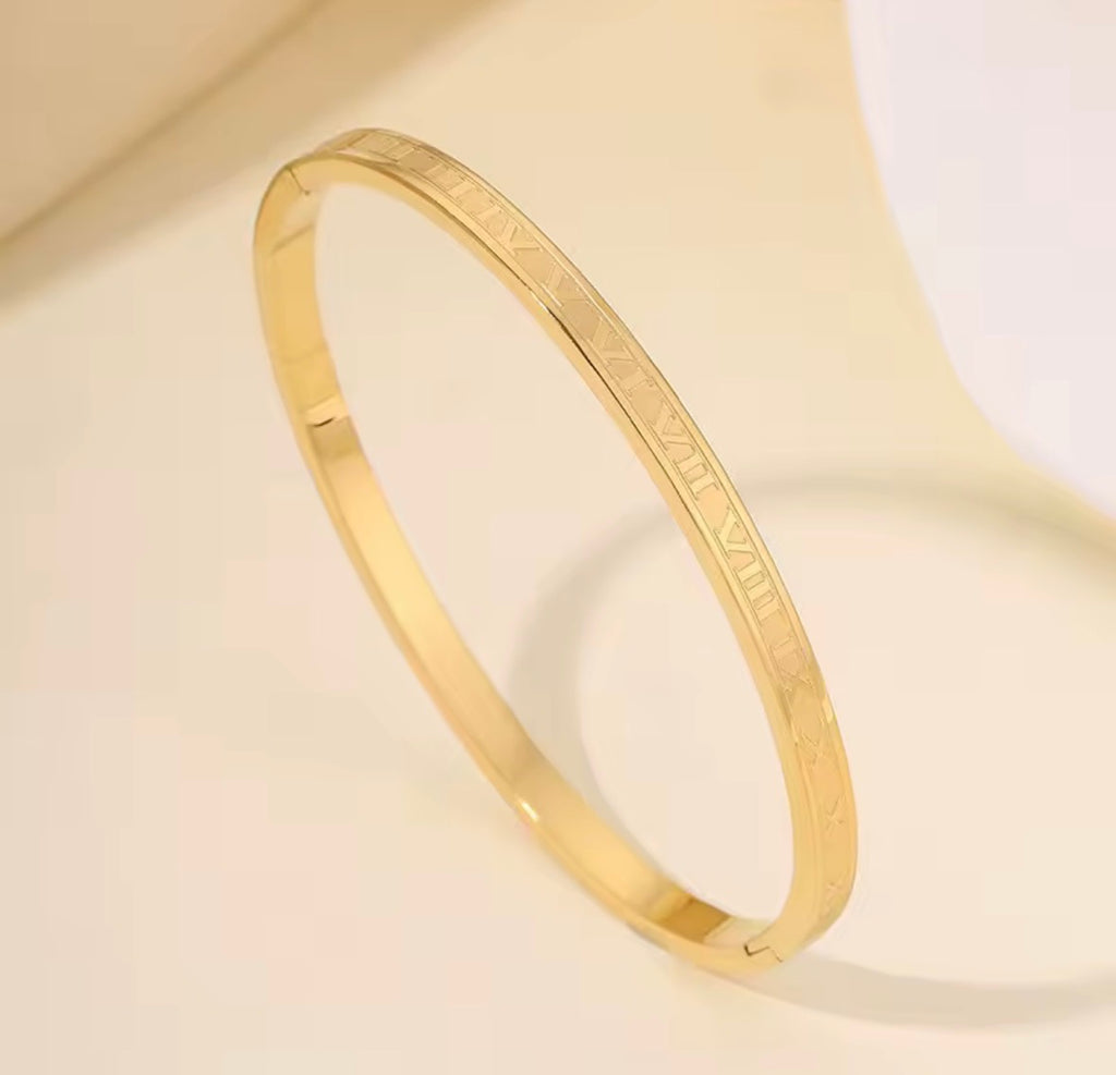 The Romanova Bangle bracelet with engraved text on a beige background