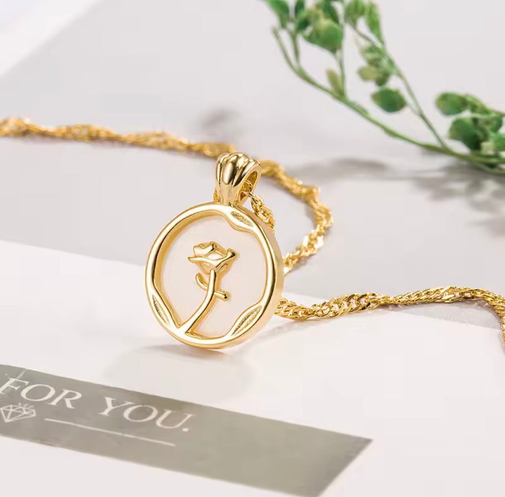 The Rosa del Mar necklace with a rose pendant on a white surface with greenery