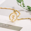 The Rosa del Mar necklace with a rose pendant on a white surface with greenery