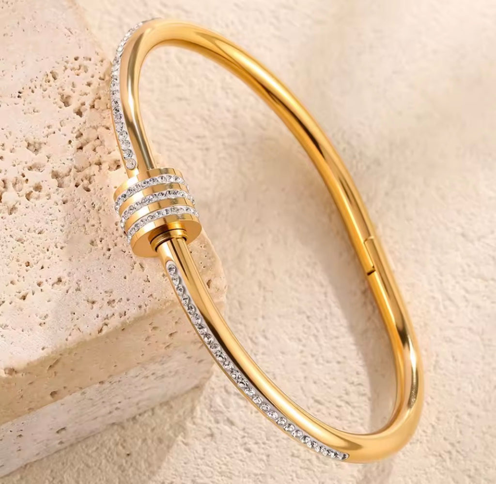  The Selene Bangle Gold bracelet with diamond accents on a beige stone background