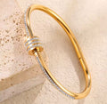  The Selene Bangle Gold bracelet with diamond accents on a beige stone background