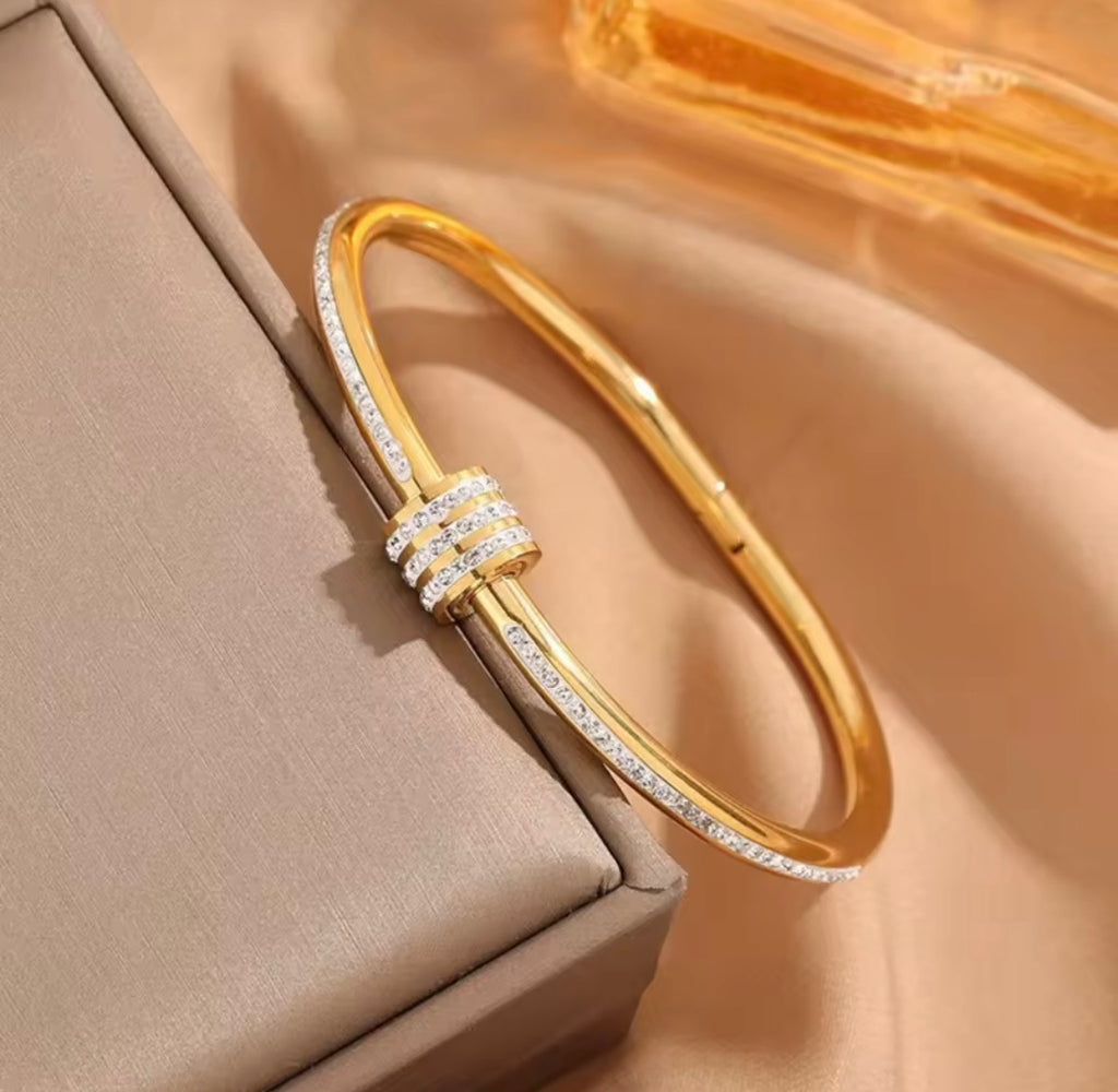 The Selene Bangle Gold bracelet with diamond accents on a beige surface