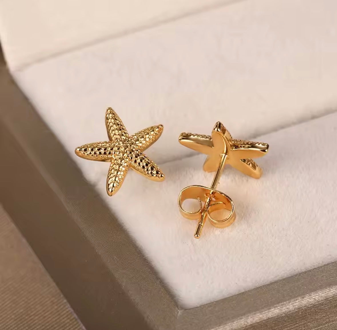  The Stella Mare Studs Gold starfish earrings on a soft beige background