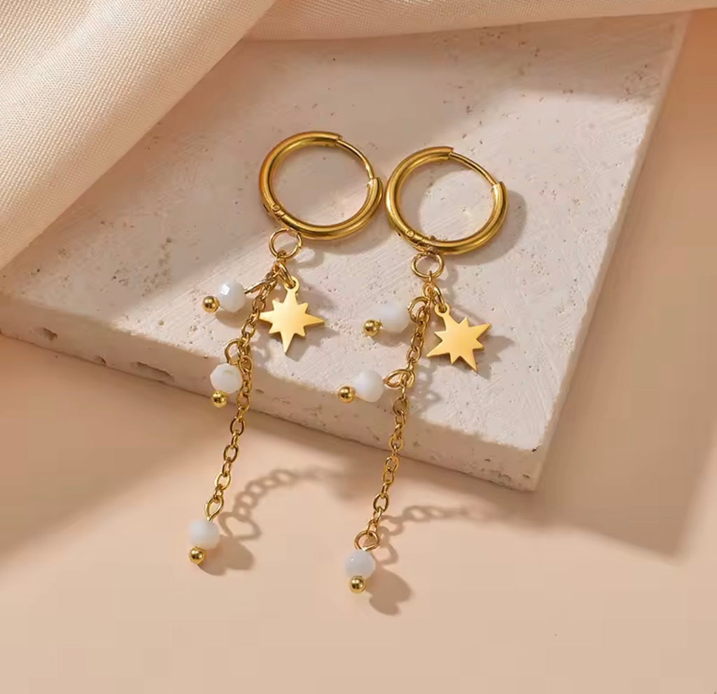 The Stella earrings Gold hoop earrings with star and pearl charms on a textured surface