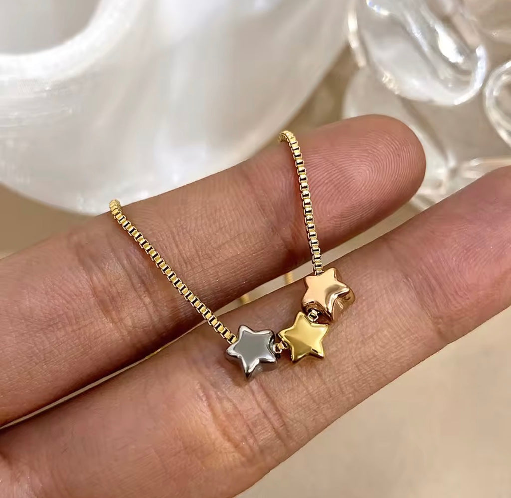 The Twinkle Necklace: Gold bracelet with star-shaped charms on a hand against a neutral background