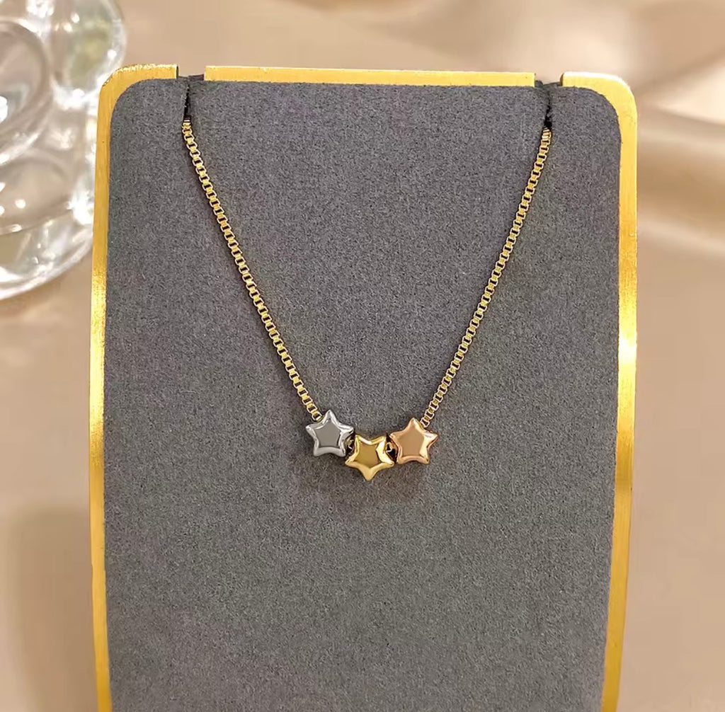 The Twinkle Necklace: Necklace with star pendants on a gray stand with gold border