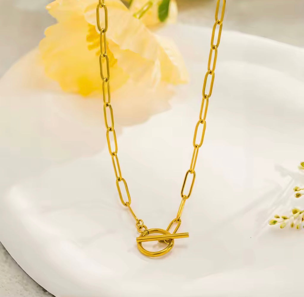 The Valiant chain necklace with a clasp on a white surface with yellow flowers.