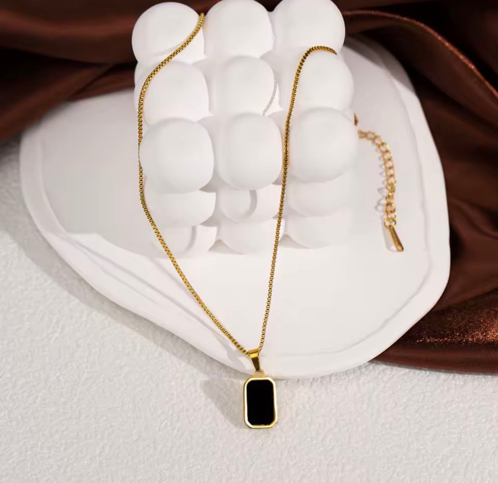 The Vertex Necklace Gold necklace with a black pendant on a white stand