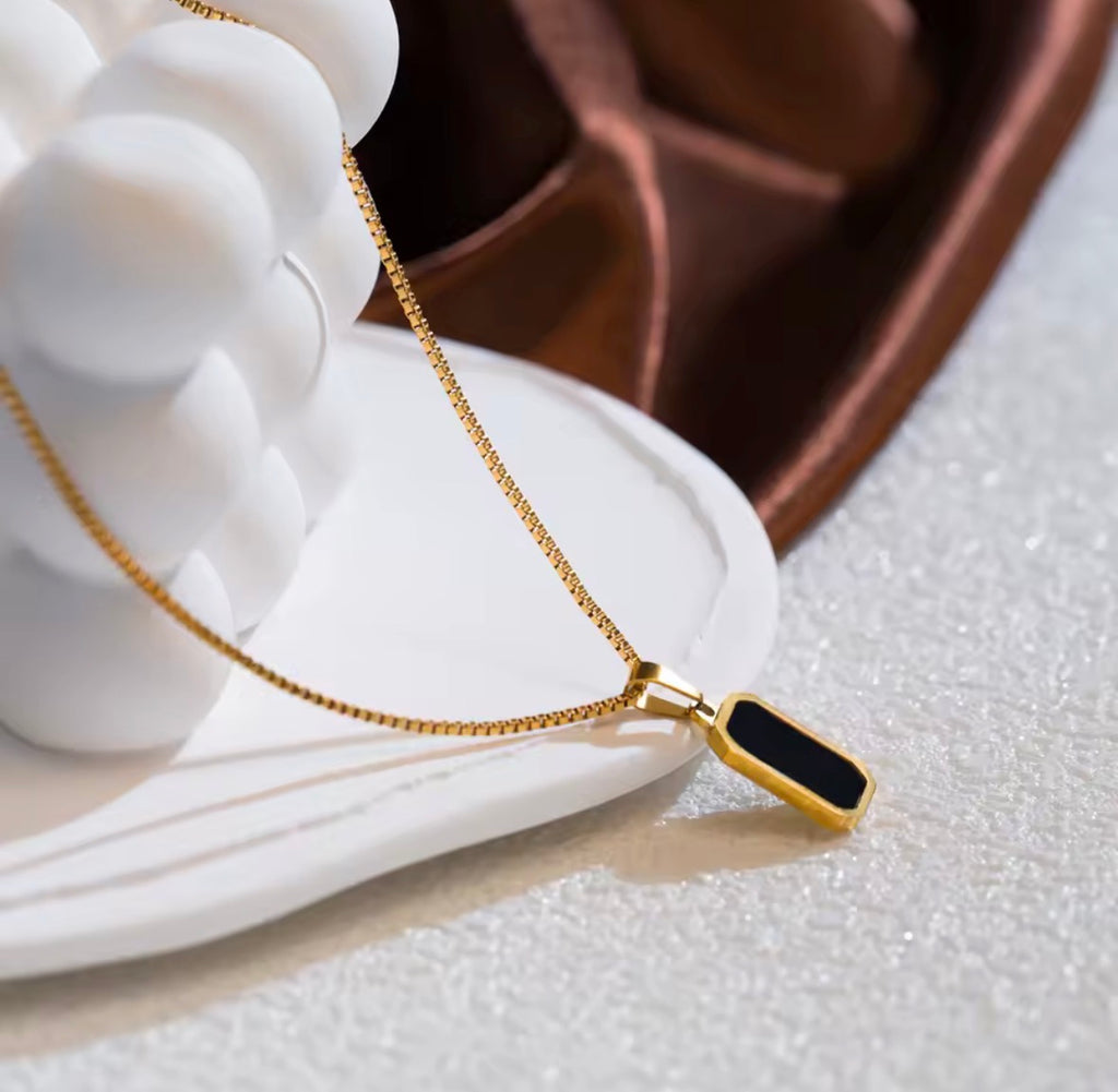 The Vertex Necklace   Gold necklace with a black pendant on a white surface