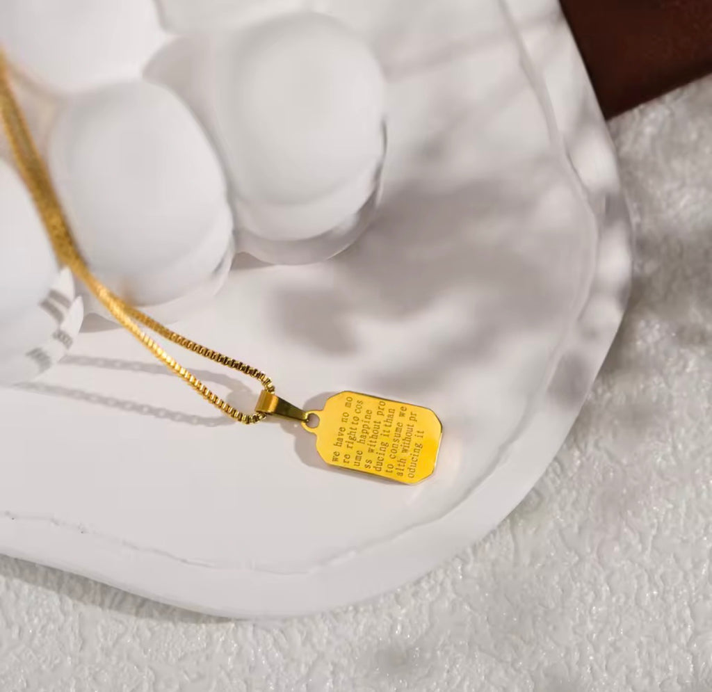 The Vertex Necklace Gold necklace with a tag on a textured white surface