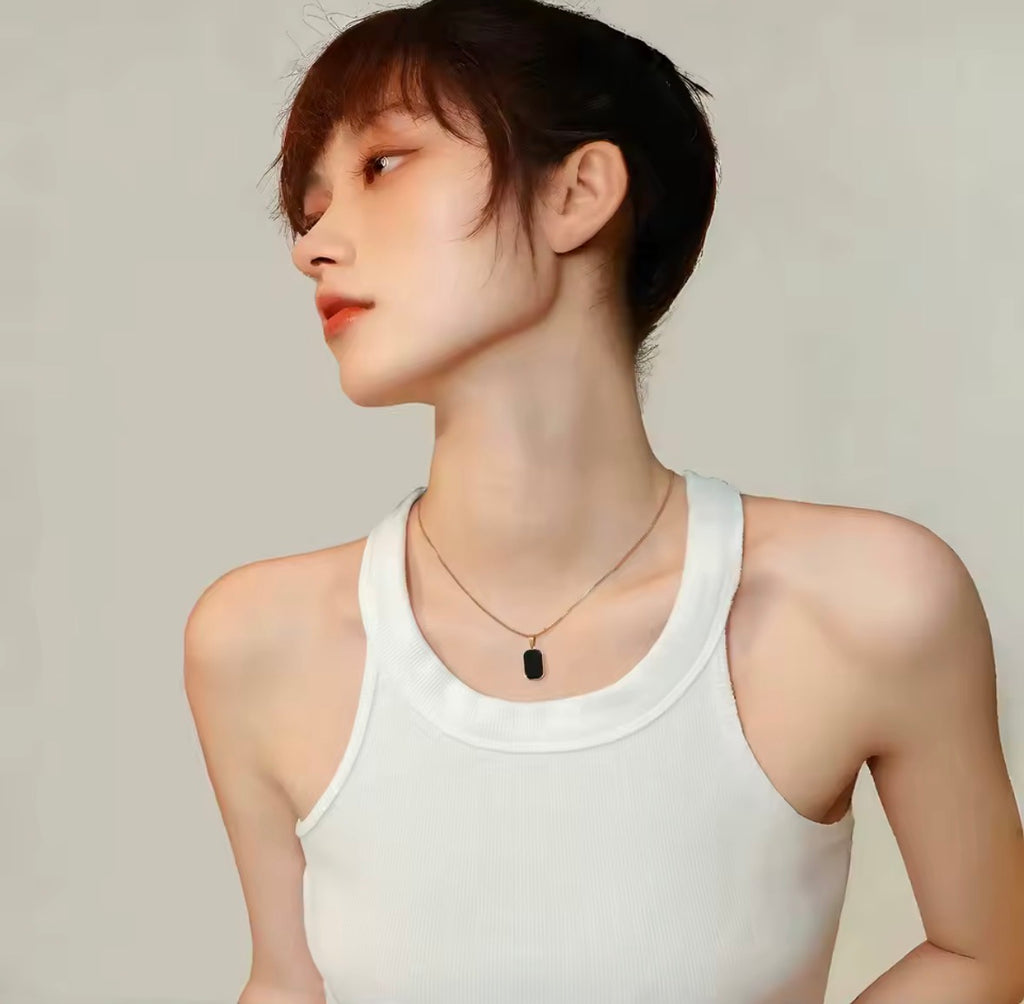 The Vertex Necklace   Person wearing a white tank top and a necklace with a black pendant on a plain background