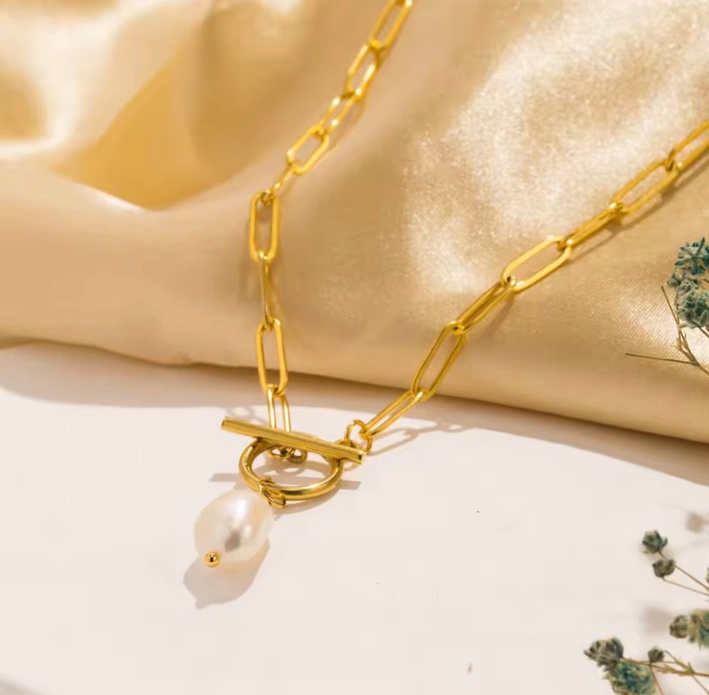 The Vivienne Pearl Gold chain necklace with a pearl pendant on a beige fabric background