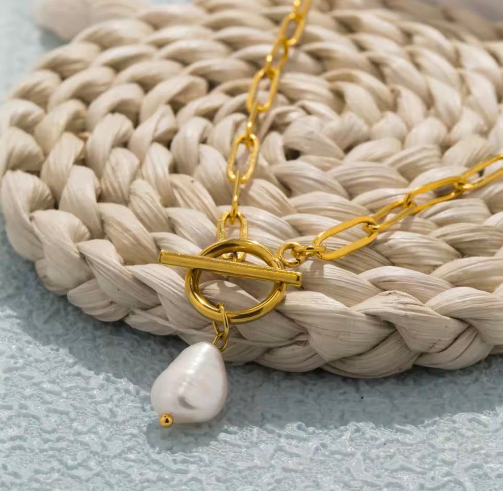 The Vivienne Pearl Gold necklace with a white pendant on a textured surface