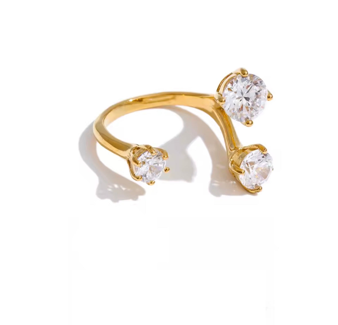 A gold ring with three round clear gemstones in a branching, open-style design, photographed on a clean white background with a soft shadow.