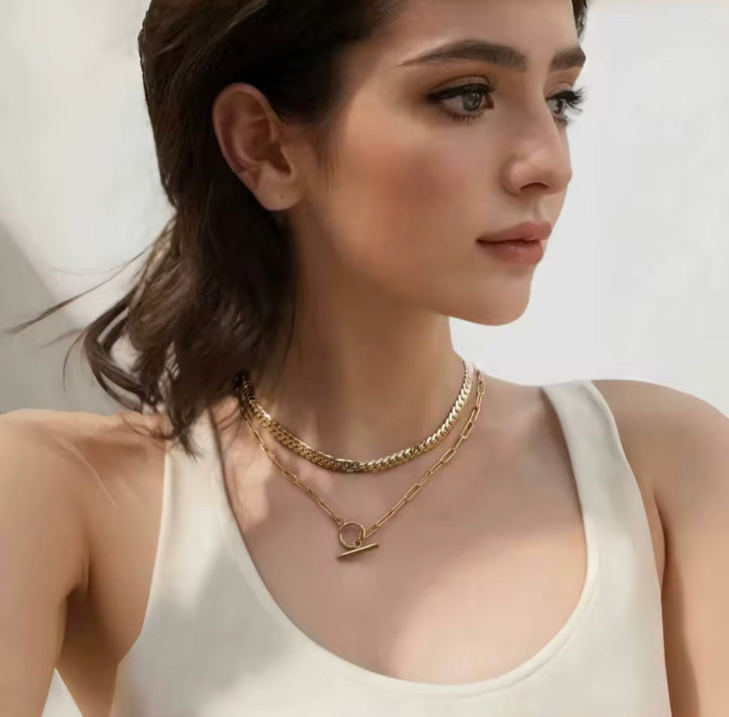 Woman wearing gold The Valiant necklaces on a plain background