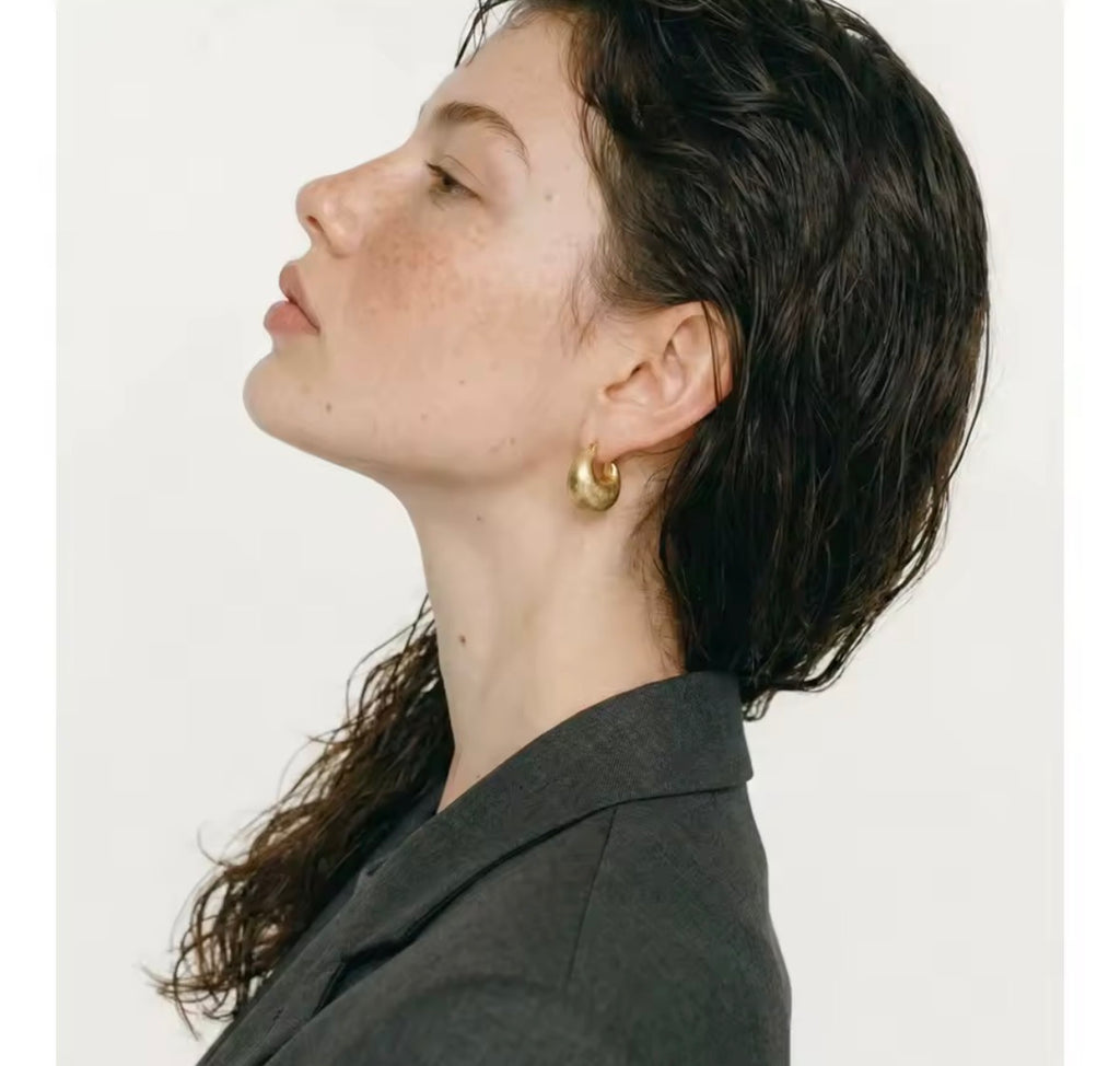 Side view of The Savara gold statement hoop earrings worn by a woman