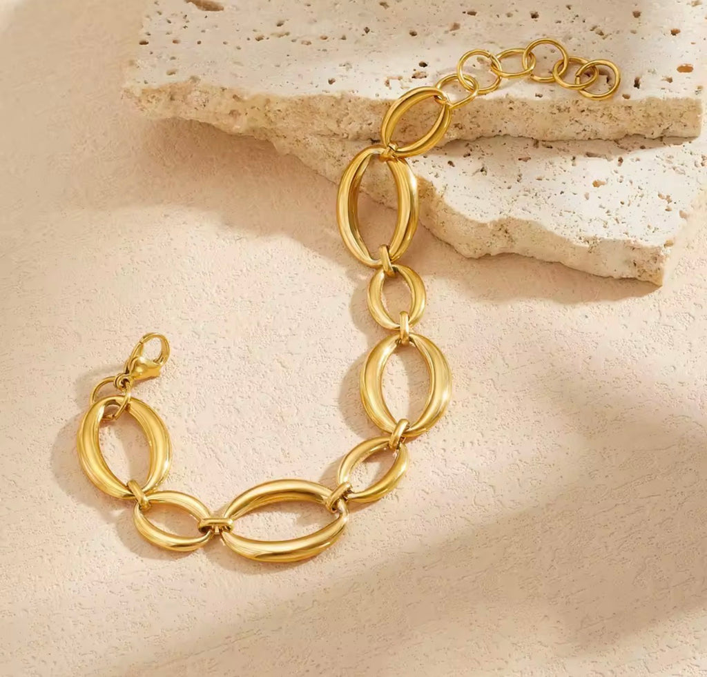 The Sorevia gold oval link bracelet on a neutral textured background